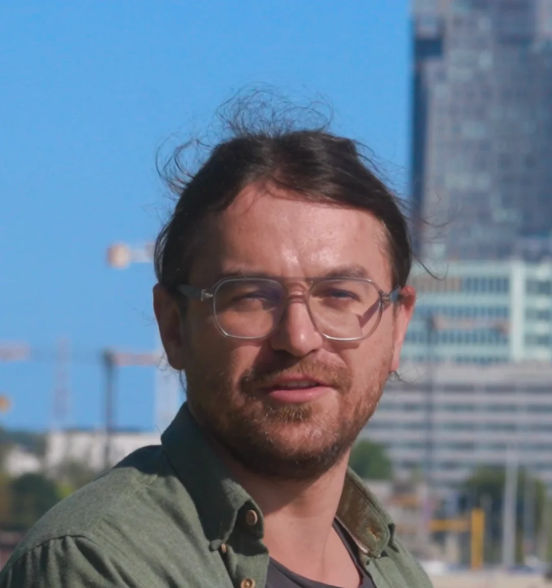 dr Przemek Fiedorczuk w zielonej koszuli, uśmiechnięty, w tle wieżowiec Sea Towers w Gdyni